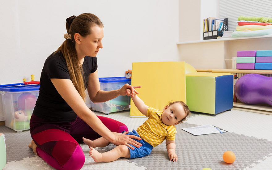 A PT works with a baby with PWS on the floor.