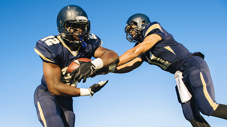 A quarterback hands off a football to a teammate.