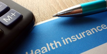 A calculator, pen, and a health insurance document on a table.