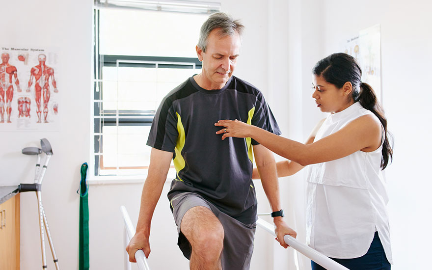 A PT works with a patient on balance training using parallel bars 