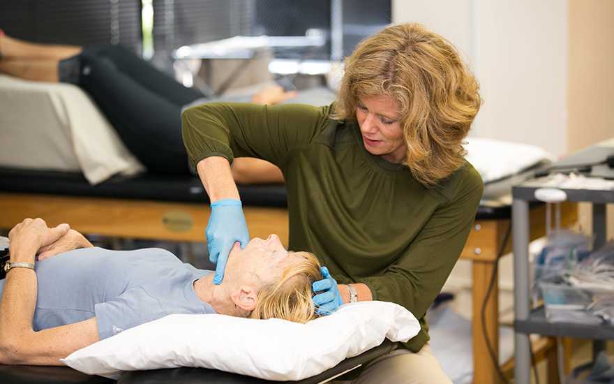 A physical therapist provides hands-on treatment on a woman's jaw.