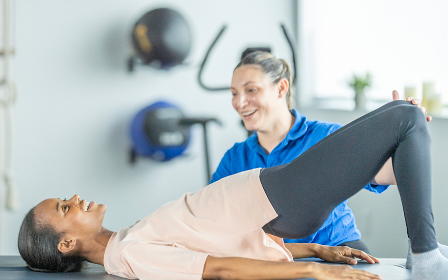 Physical therapist guiding a Black client through a bridge exercise to strengthen the hips and support recovery from knee pain and conditions like plica syndrome