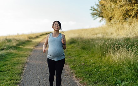 A pregnany woman walking briskly on an outdoor trail.