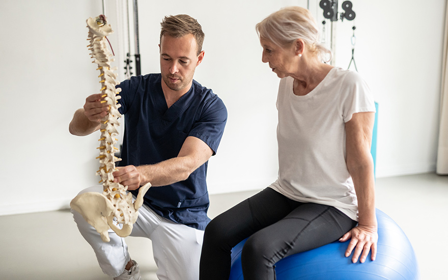 A physical therapist (PT) shows a patient a model of a spine to educate them on their condition