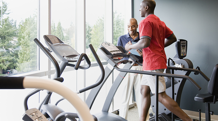 A man running on a treadmill as his physical therapist looks on.