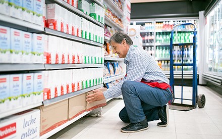 A grocery worker squatting  and placing a box of back stock on a grocery shelf