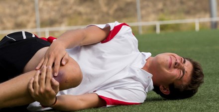 Youth athlete with a knee injury holds his knee on the soccer field.