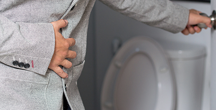 A person standing by the toilet holding their stomach.