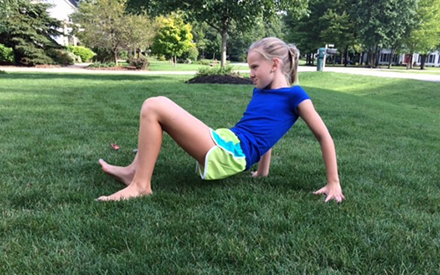 A young person doing the crab walk activity on the grass 
