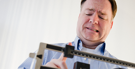 Man standing on scale grimacing.
