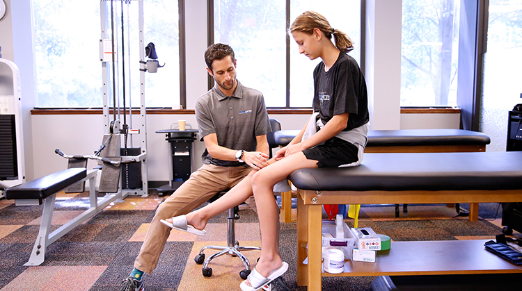A physical therapist examines a young girl's knee.