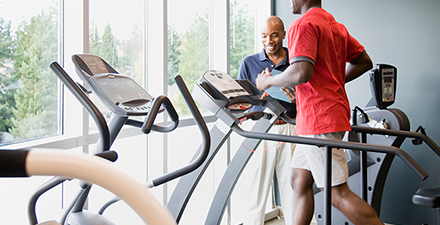 A man running on a treadmill as his physical therapist looks on.