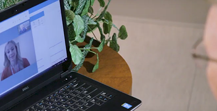 Physical therapist on laptop screen instructing a patient.