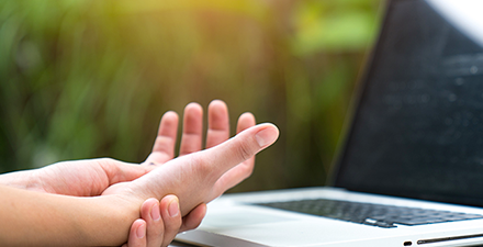 Person holding their wrist in pain in front of a computer.